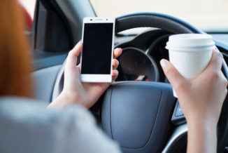 A Woman drinking coffee and texting while driving