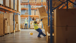 a man in a warehouse, in an out balance position where a stock of boxes might fell on him - dangerous warehouse work -