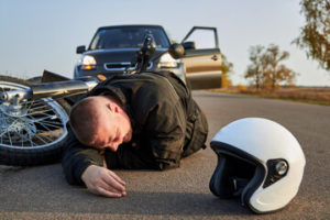 A motorcyclist lies on the asphalt near a motorcycle and car