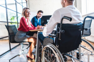 Partial view of smiling business people looking at colleague in wheelchair in office