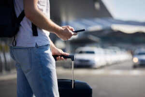 a man holding his phone and a travel bags waiting for ridesharing vehicle