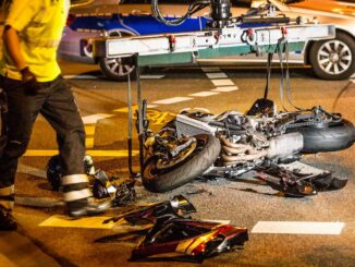 A motorcycle rider is involved in an accident on the road, with their motorcycle laying on its side and debris scattered around the scene.