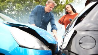 A man (left side) and a woman are looking at their cars after a crash.