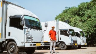 Three delivery trucks and a courier standing between the trucks.